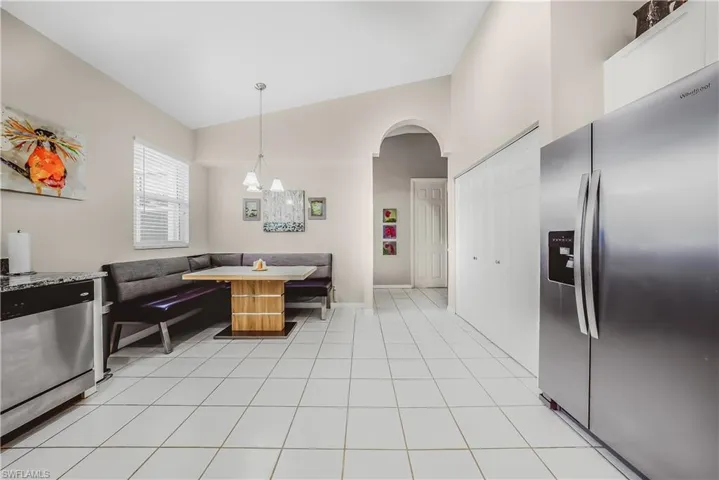 Kitchen with stainless steel appliances, arched walkways, light tile patterned floors, hanging light fixtures, and high vaulted ceiling