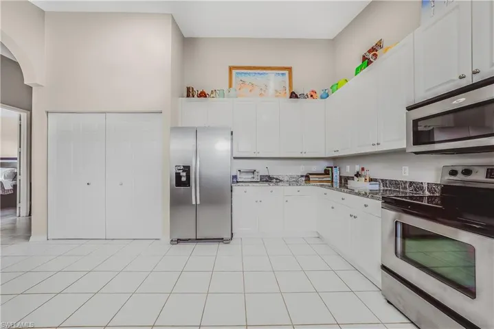Kitchen featuring stainless steel appliances, white cabinets, dark stone countertops, light tile patterned flooring, and a towering ceiling