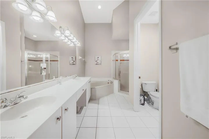 Bathroom featuring light tile patterned floors, a stall shower, double vanity, and a garden tub
