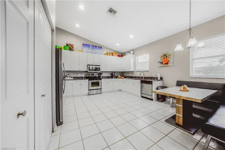 Kitchen with vaulted ceiling, pendant lighting, stainless steel appliances, white cabinets, and light tile patterned flooring