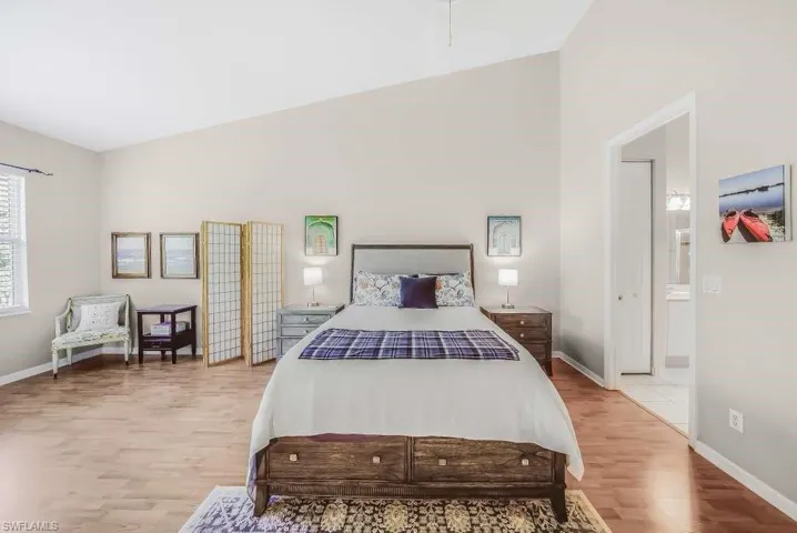 Bedroom featuring light wood-style floors, high vaulted ceiling, and ensuite bath