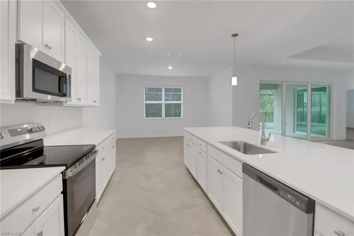 Kitchen with decorative light fixtures, light countertops, appliances with stainless steel finishes, white cabinets, and a sink