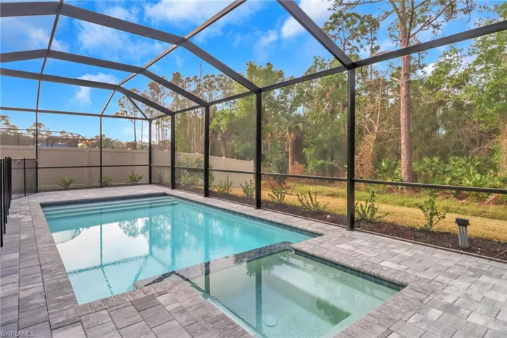 View of pool with glass enclosure, a pool with connected hot tub, and a patio