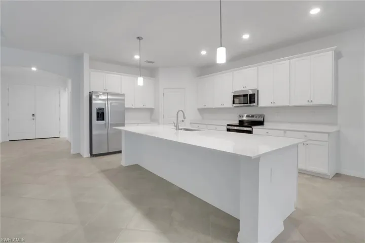 Kitchen with a center island with sink, appliances with stainless steel finishes, decorative light fixtures, light countertops, and a sink