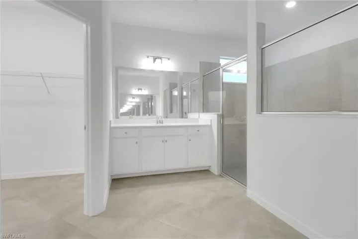 Full bathroom with a stall shower, a walk in closet, vanity, and baseboards
