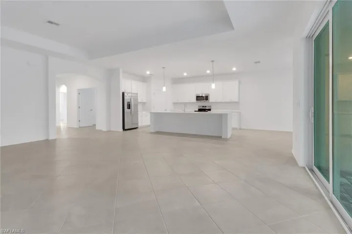 Unfurnished living room with arched walkways, light tile patterned flooring, recessed lighting, visible vents, and a raised ceiling
