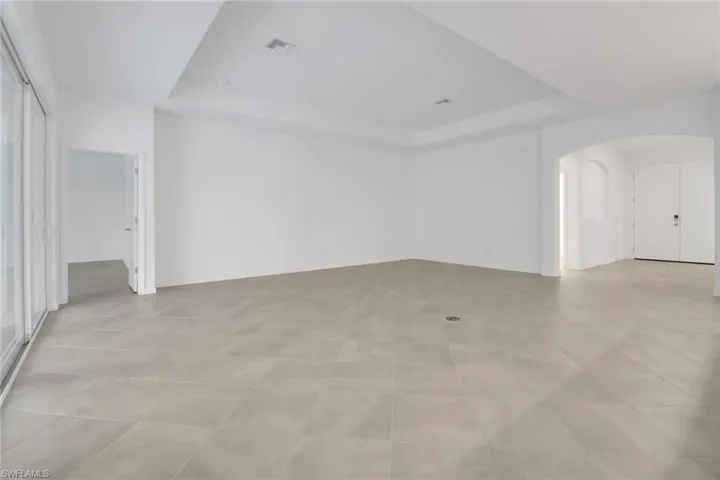 Empty room featuring a tray ceiling, visible vents, and arched walkways