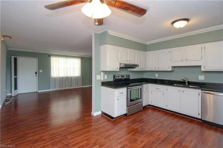 Kitchen with stainless steel appliances, dark hardwood / wood-style flooring, crown molding, white cabinetry, and ceiling fan