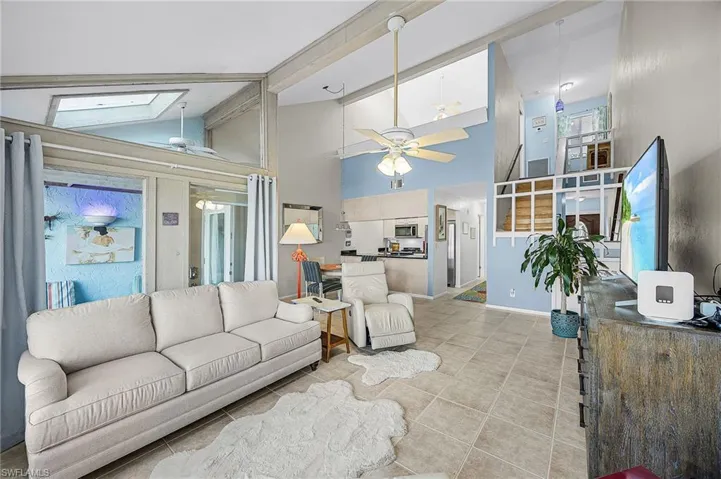 Living room with a ceiling fan, high vaulted ceiling, tile patterned flooring, and a skylight