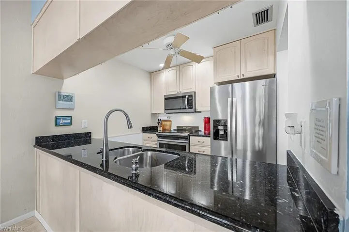 Kitchen with stainless steel appliances, dark stone countertops, a ceiling fan, and light brown cabinets