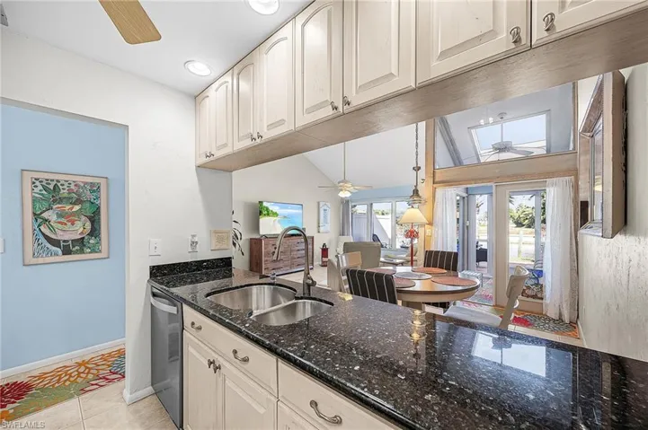 Kitchen with a ceiling fan, dark stone counters, vaulted ceiling, light tile patterned flooring, and dishwasher