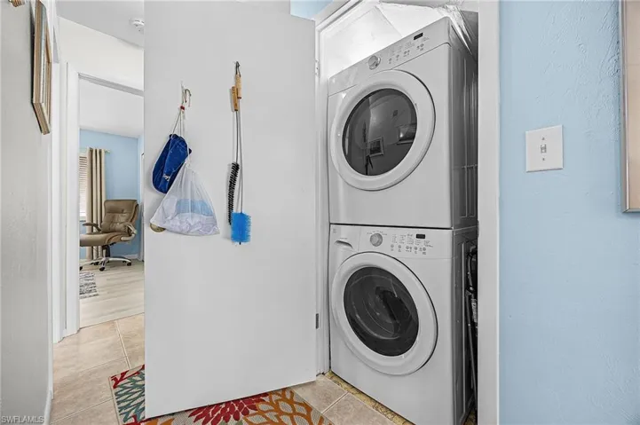 Laundry room with stacked washing machine and dryer and light tile patterned floors