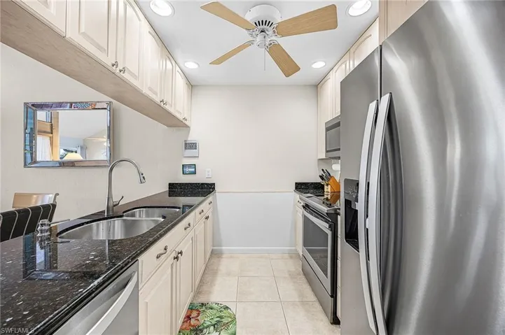 Kitchen featuring stainless steel appliances, dark stone countertops, recessed lighting, light tile patterned flooring, and a ceiling fan