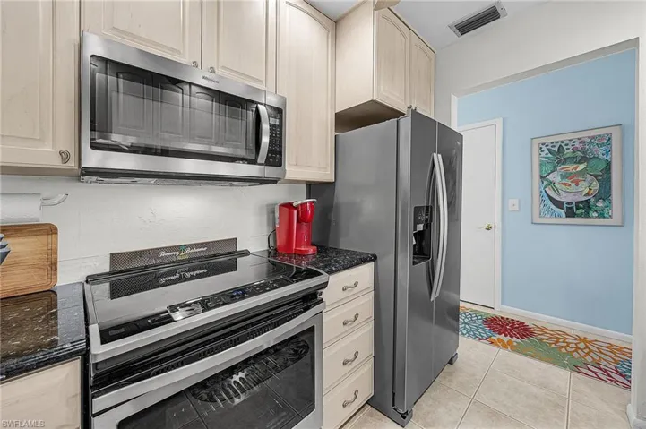Kitchen with appliances with stainless steel finishes, dark stone counters, light tile patterned floors, and light brown cabinetry