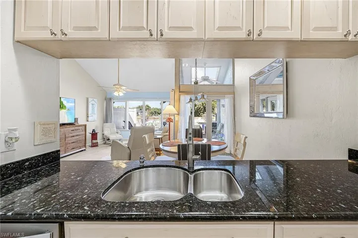 Kitchen with a textured wall, dark stone countertops, open floor plan, lofted ceiling, and a ceiling fan