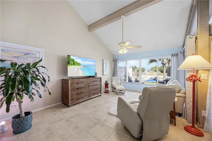 Living area featuring high vaulted ceiling, beam ceiling, tile patterned flooring, and a ceiling fan