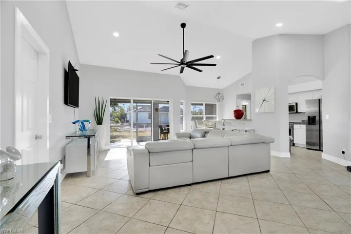 Living room with light tile patterned flooring, high vaulted ceiling, visible vents, baseboards, and ceiling fan