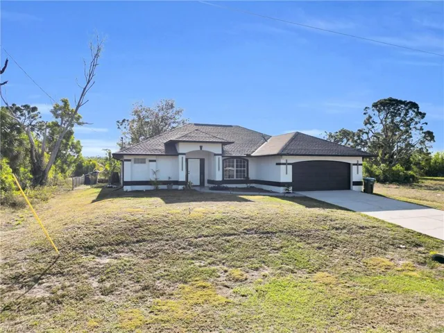 View of front of property with concrete driveway, stucco siding, fence, an attached garage, and a front lawn