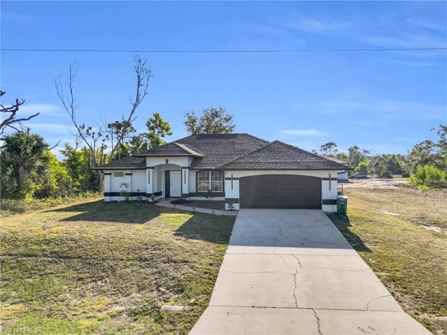 View of front facade featuring a front lawn, stucco siding, a garage, and concrete driveway