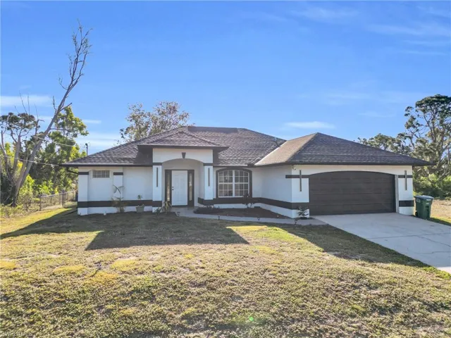 View of front of home featuring stucco siding, fence, driveway, a front lawn, and a garage