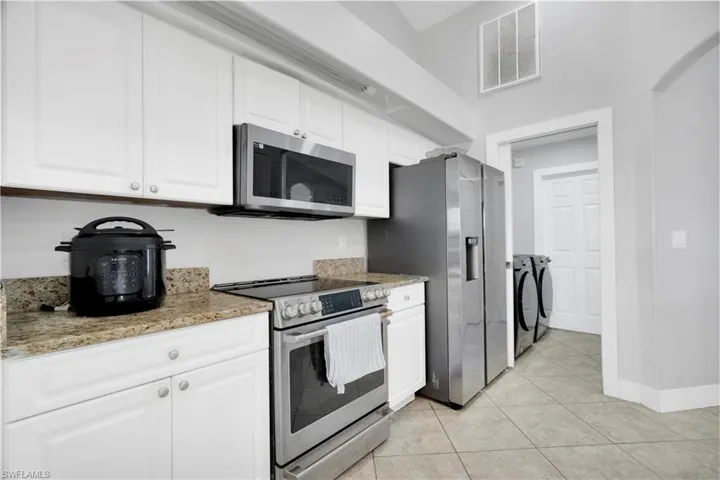 Kitchen featuring white cabinetry, appliances with stainless steel finishes, washer and dryer, and visible vents