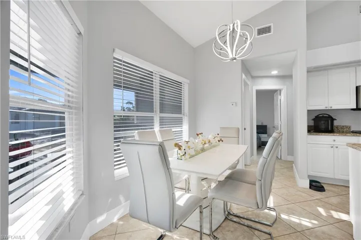 Dining room featuring a notable chandelier, lofted ceiling, light tile patterned floors, baseboards, and visible vents