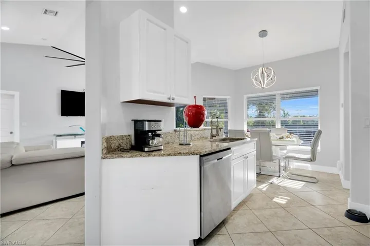 Kitchen featuring light tile patterned flooring, light stone countertops, white cabinetry, a sink, and stainless steel dishwasher