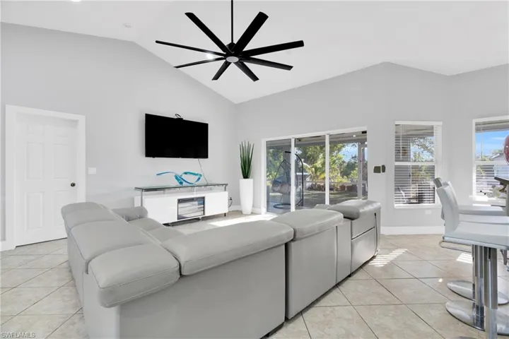 Living area featuring light tile patterned floors, high vaulted ceiling, baseboards, and ceiling fan