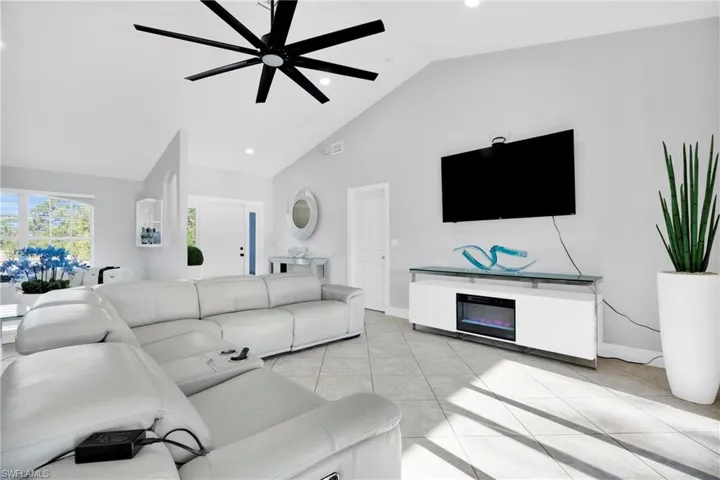 Living room with light tile patterned flooring, baseboards, high vaulted ceiling, and a ceiling fan