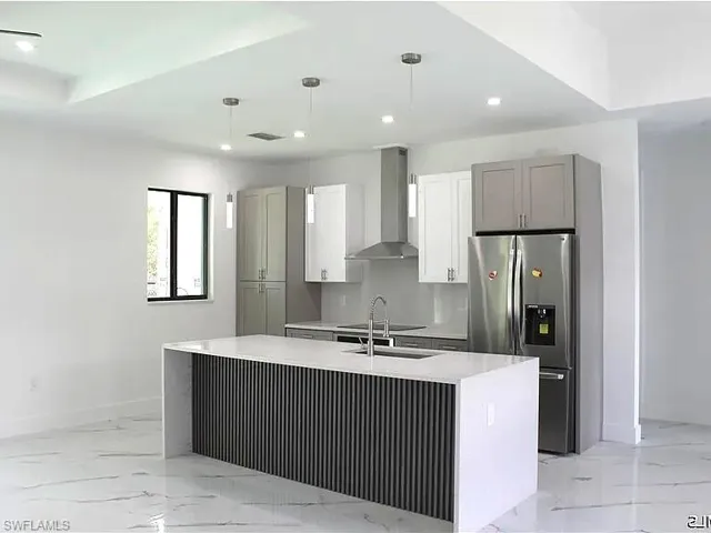 Modern kitchen featuring a waterfall island with slatted detailing, recessed and pendant lighting, stainless steel appliances, and two-tone cabinetry