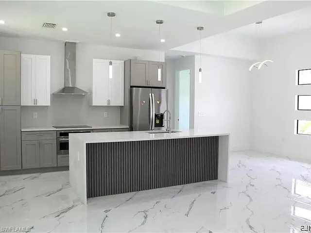 Open-concept kitchen featuring an island with a waterfall countertop, integrated sink, and modern pendant lighting
