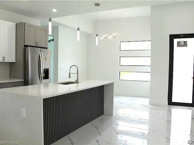 Modern kitchen with a large island featuring a waterfall countertop and a fluted wood-finish panel