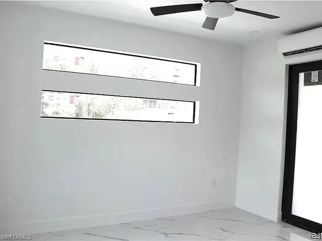 White-walled interior with a ceiling fan, two horizontal windows, and a black-framed door