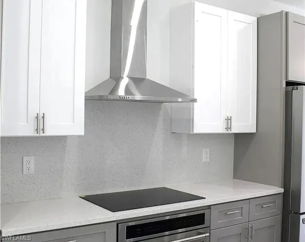Modern kitchen featuring white upper cabinetry, gray lower cabinetry, and a stainless steel range hood