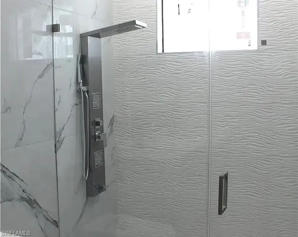 Shower enclosure featuring a multi-function shower panel with an overhead rain shower and handheld sprayer