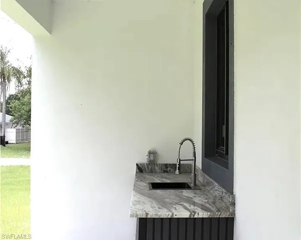 Outdoor kitchen area featuring a dark stone countertop, black undermount sink, and a high-arc pull-down faucet