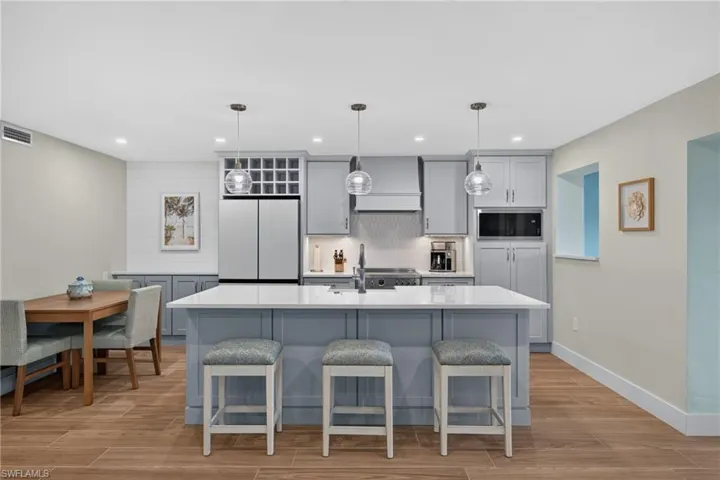 Kitchen featuring a center island with seating, pendant lighting, stainless steel appliances, light gray cabinetry, and wood-finish flooring