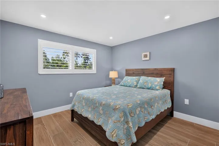 Recessed lighting, wood-finish flooring, white window shutters, and a wood-paneled headboard