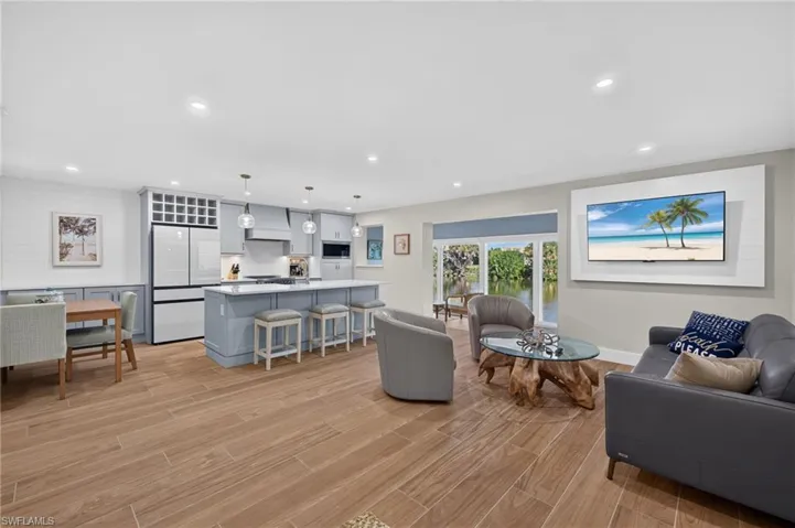 Wood-finish flooring throughout, light-toned cabinetry with a built-in wine rack, kitchen island with seating, recessed lighting, and a prominent water feature visible through large glass doors