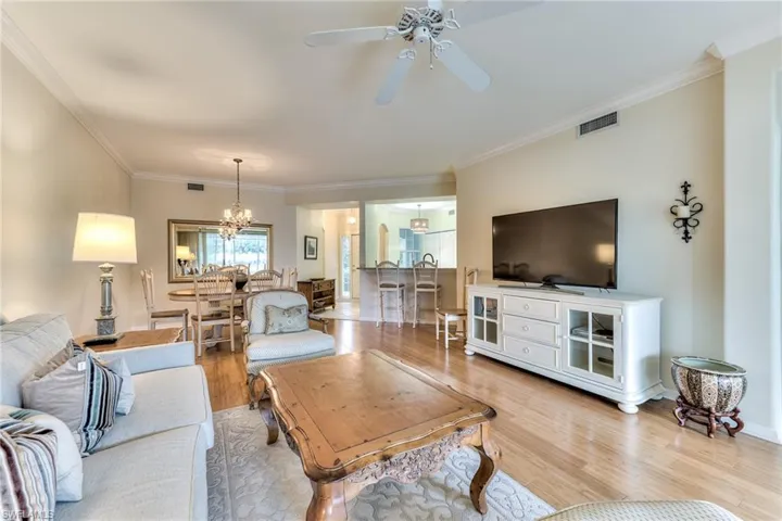 Living room with ornamental molding, ceiling fan with notable chandelier, and light wood-type flooring