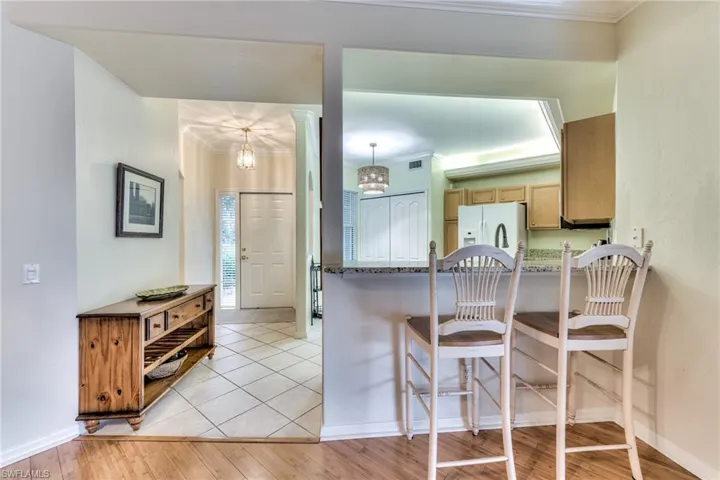 Kitchen with light wood-type flooring, white fridge with ice dispenser, ornamental molding, and a notable chandelier