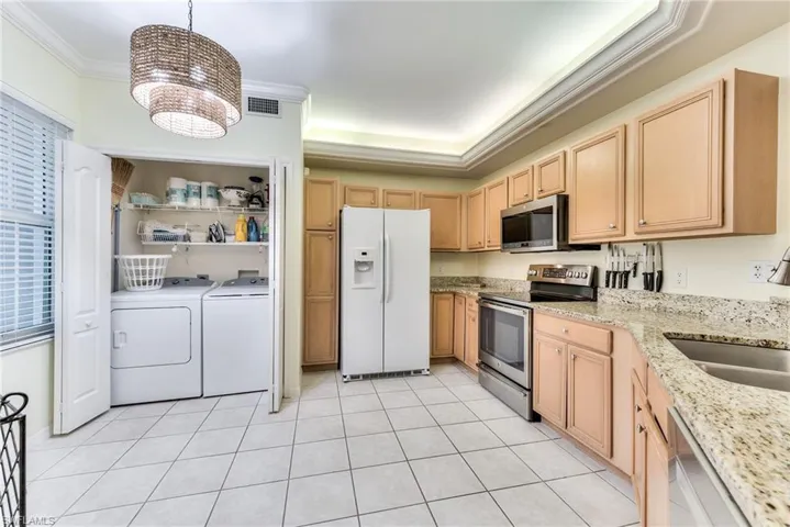 Kitchen featuring appliances with stainless steel finishes, washer and dryer, light brown cabinets, a chandelier, and hanging light fixtures