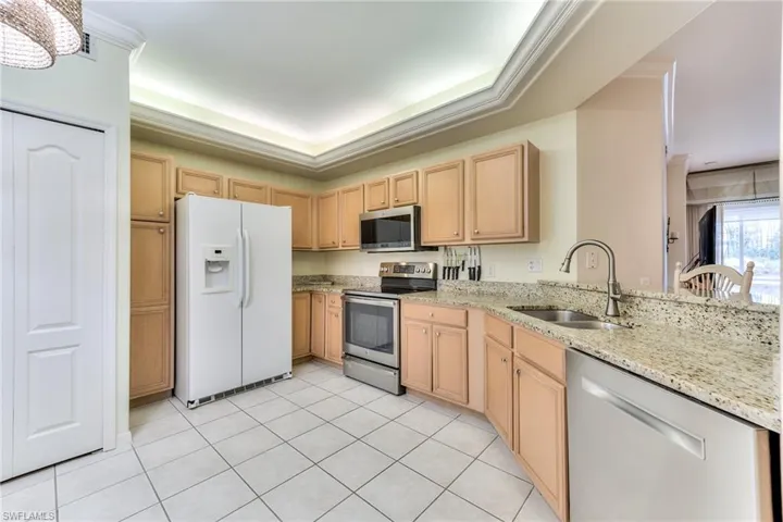 Kitchen featuring appliances with stainless steel finishes, a tray ceiling, light tile patterned floors, and sink