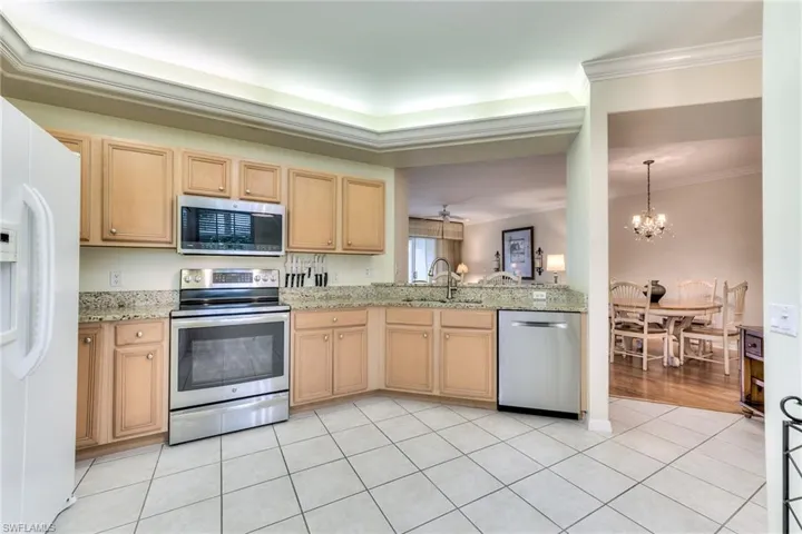 Kitchen with appliances with stainless steel finishes, crown molding, sink, light tile patterned floors, and a chandelier