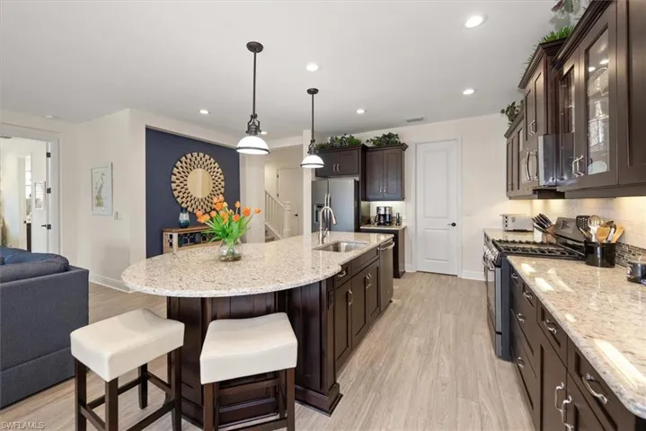 Kitchen with appliances with stainless steel finishes, dark brown cabinetry, a sink, light wood-style flooring, and open floor plan