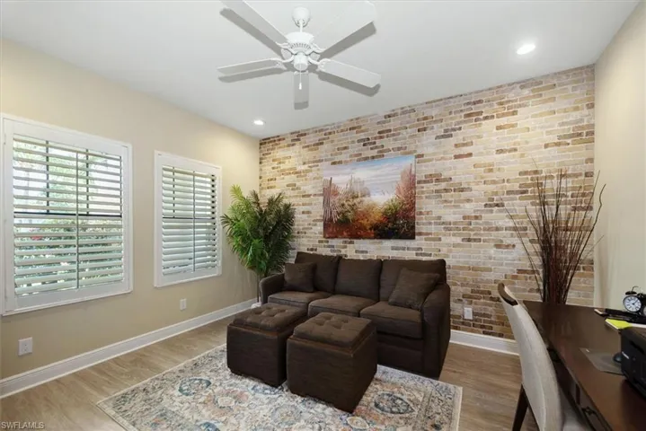 Den with brick wall, baseboards, wood finished floors, ceiling fan, and an accent wall