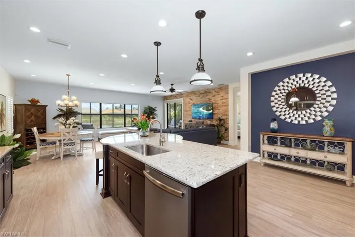 Kitchen featuring dishwasher, a sink, light wood-style floors, dark brown cabinetry, and light stone countertops