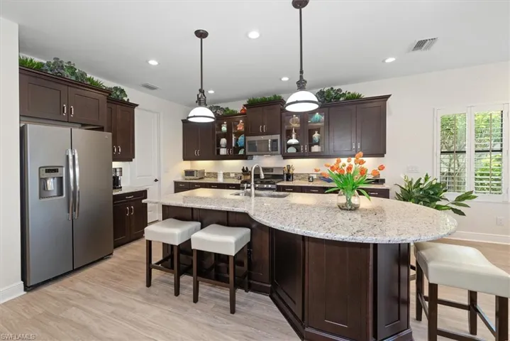 Kitchen with appliances with stainless steel finishes, a sink, light wood-style floors, dark brown cabinets, and recessed lighting