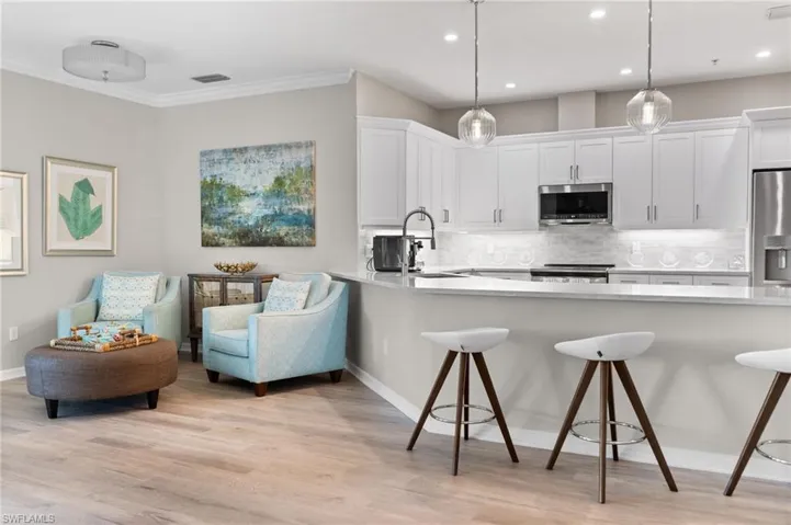 Kitchen with a breakfast bar area, light wood-type flooring, stainless steel appliances, hanging light fixtures, and white cabinets