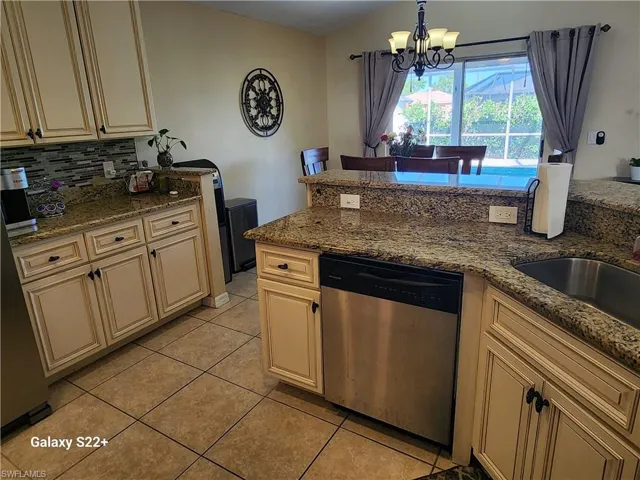 Kitchen featuring pendant lighting, tasteful backsplash, stainless steel dishwasher, light tile patterned floors, and light stone counters